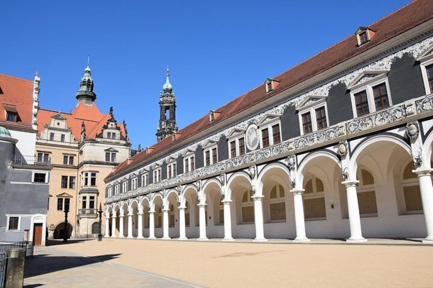 A courtyard with a building featuring arched walkways and a clock tower. 5