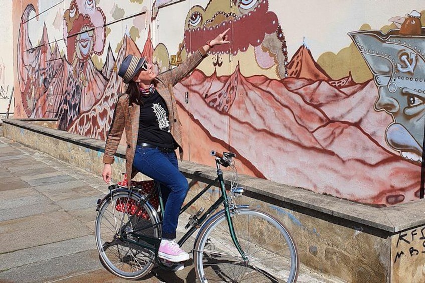 A person sitting on a bicycle in front of a mural. 4