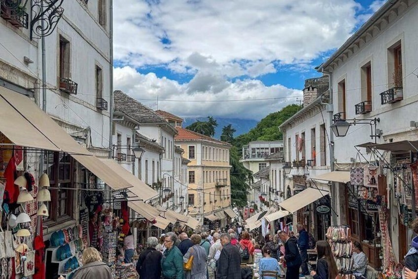 A crowded street market with white buildings and people browsing stalls. 3