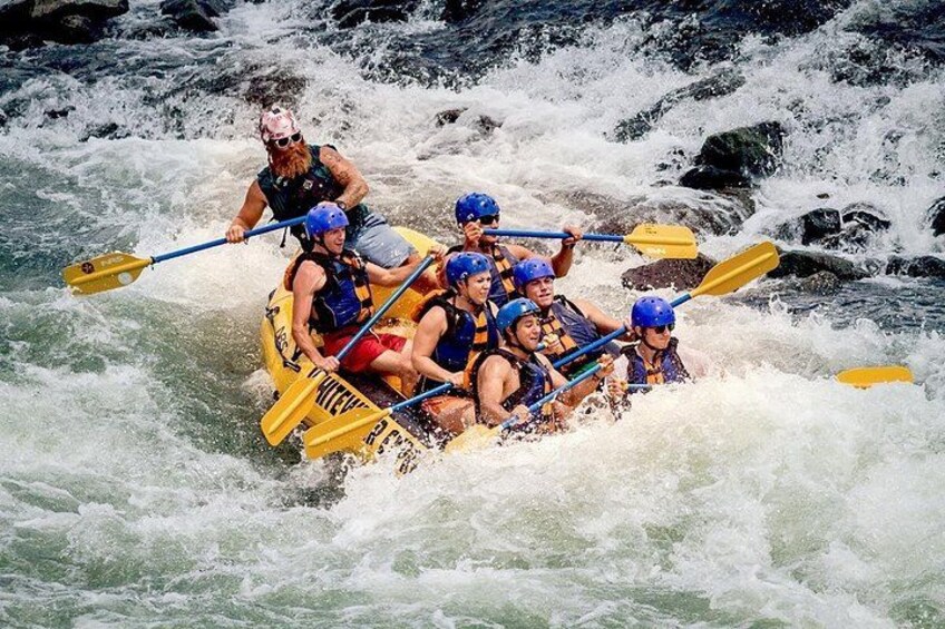 A group of people in a yellow raft navigating through white water rapids. 1