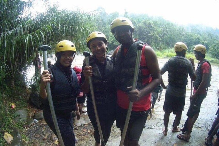 People wearing helmets and life jackets, holding paddles, standing by a river. 2