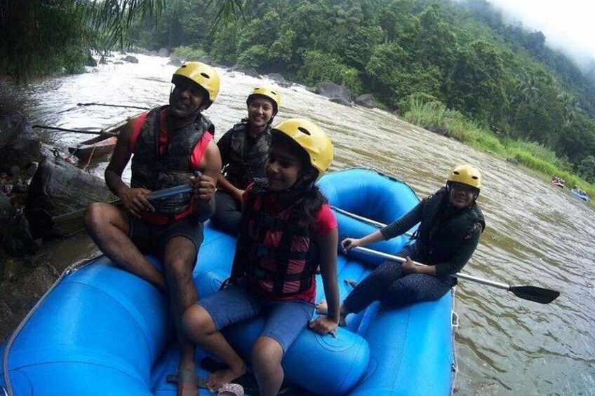 Four people on a blue inflatable raft with helmets, on a river surrounded by greenery. 3