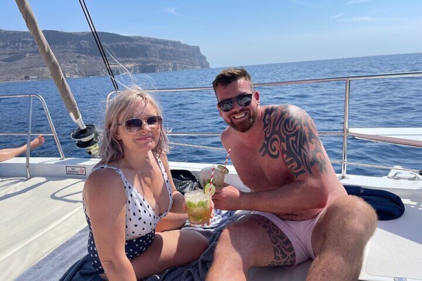 Dos personas en un velero con vistas despejadas al mar y acantilados lejanos. 4
