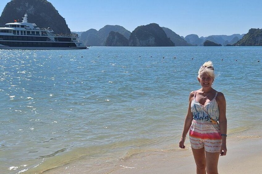 A person standing on a beach with a boat in the background and mountains in the distance. 2