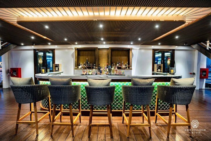 Een bar met een houten vloer, groene gestreepte krukken en een bargedeelte met flessen. 3