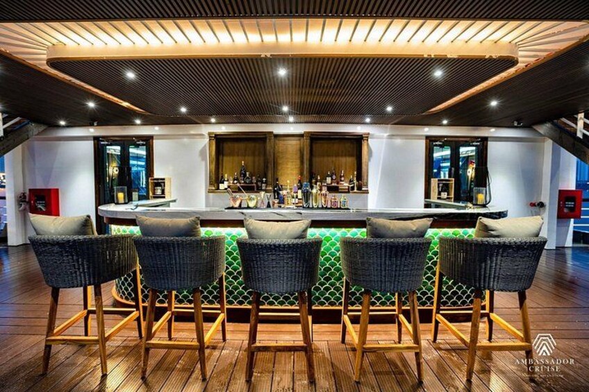 Un espace bar avec un plafond en bois, un comptoir décoré de motifs verts et des chaises en osier. 4