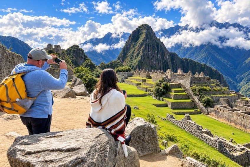 A person taking a photo of Machu Picchu ruins with a backpack, another person sitting nearby, and a mountainous landscape in the background. 1