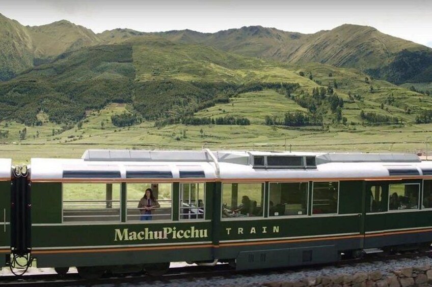 A green and white train with 'MachuPicchu TRAIN' written on it, traveling through a mountainous landscape. 5