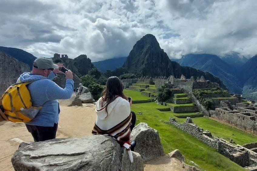A person taking a photo of Machu Picchu ruins with a mountain in the background. 1