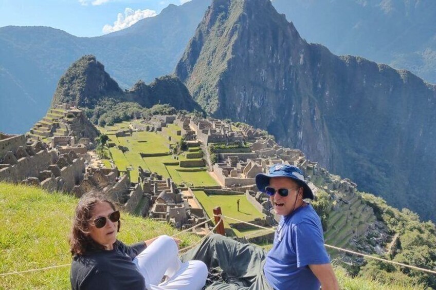Two people sitting on a grassy hill overlooking Machu Picchu. 2