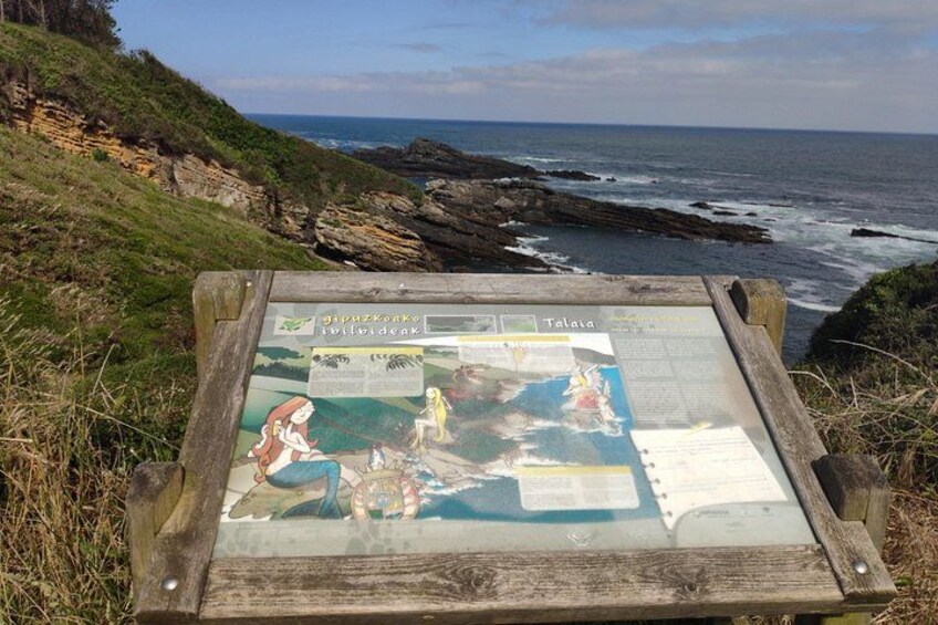A wooden sign with maps and illustrations, located by a rocky coastline with the ocean in the background. 4