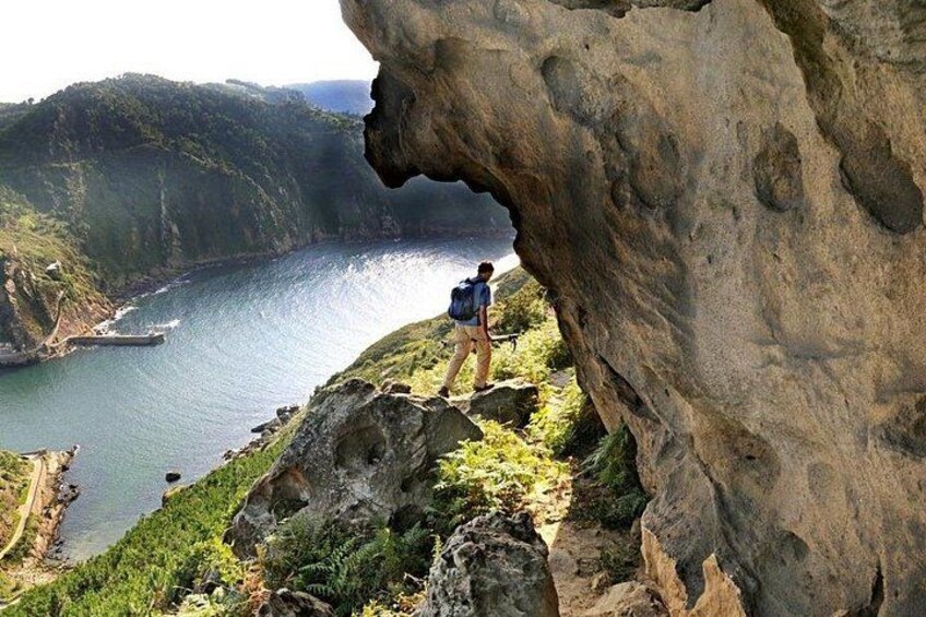 A hiker on a rocky cliff overlooking a body of water with a large rock formation in the foreground. 1