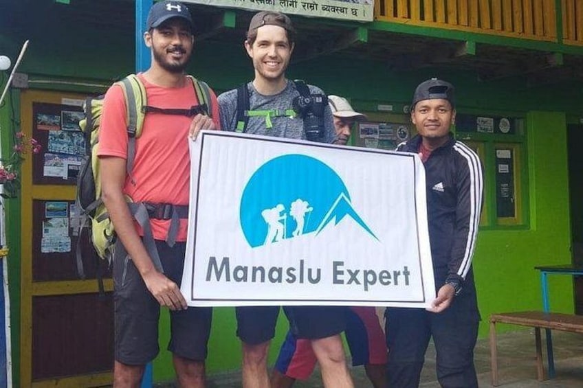 Tre personer håller i en skylt med Manaslu Experts logotyp. 3