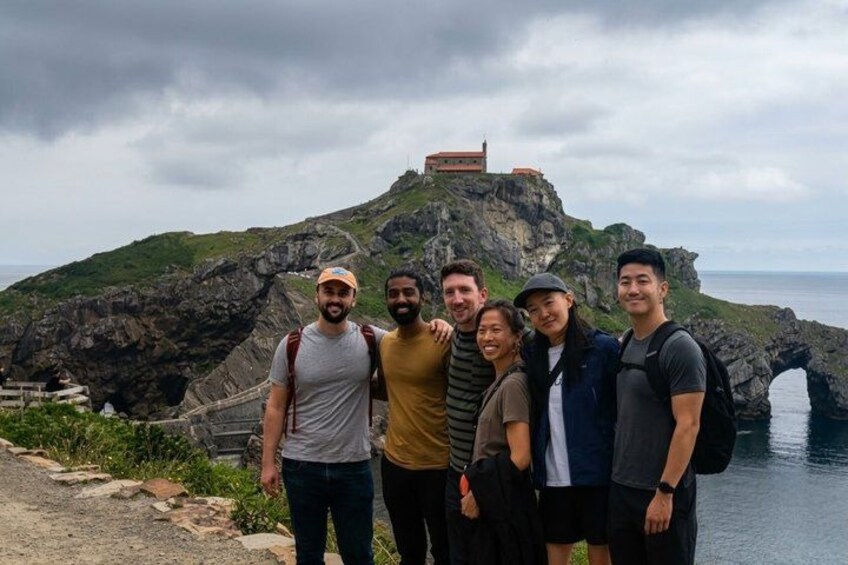 A group of people standing on a rocky cliff with a sea view and a building in the background. 4