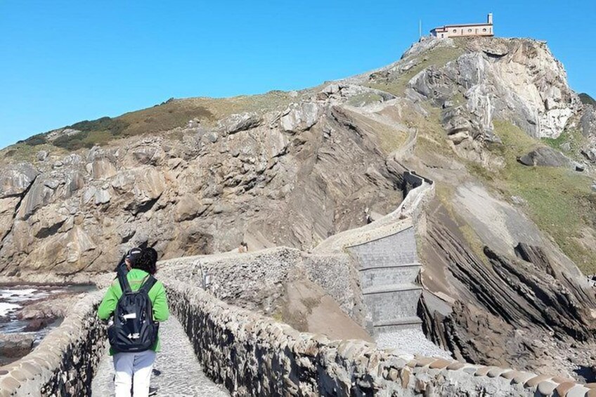 A hiker on a rocky trail with a building on a hill in the background. 2
