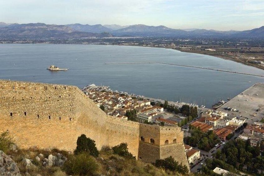 Una ciudad costera con una imponente fortaleza de piedra, un puerto deportivo y un puente a lo lejos. 5