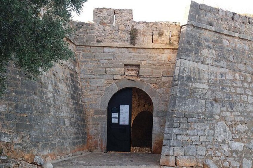 Un arco de piedra que da entrada a un edificio, con una placa en la pared y un árbol a la izquierda. 3