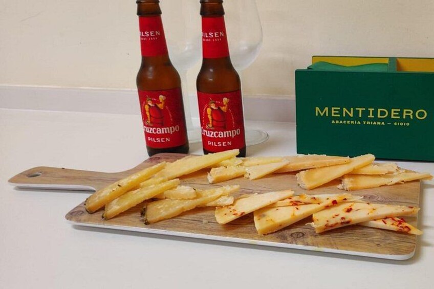 Due bottiglie di birra Cruzcampo, un tagliere di legno con formaggio e una scatola di formaggio Mentidero. 3