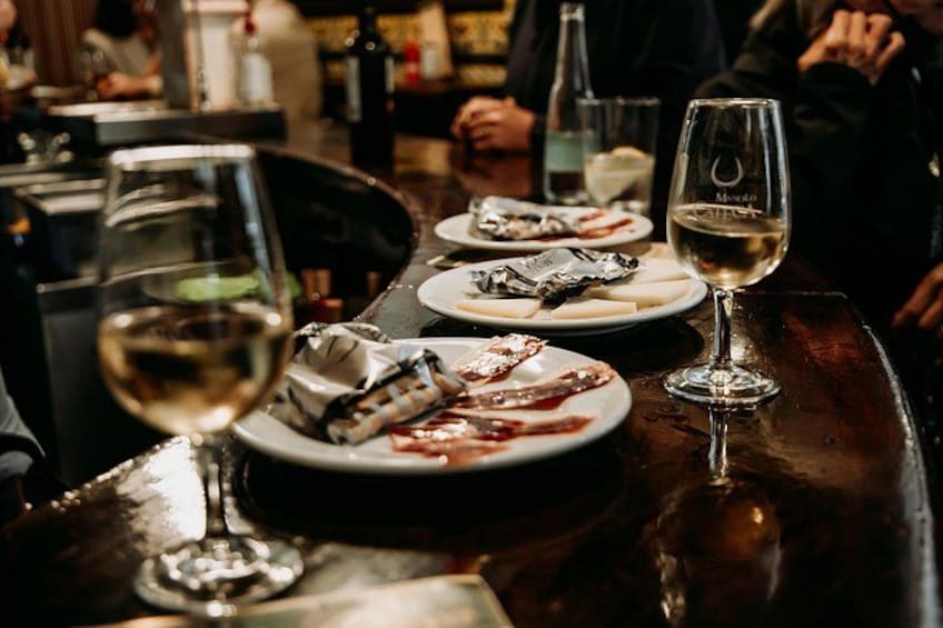 Un'ambientazione da bar con un tavolo, bicchieri da vino e piatti di cibo. 4