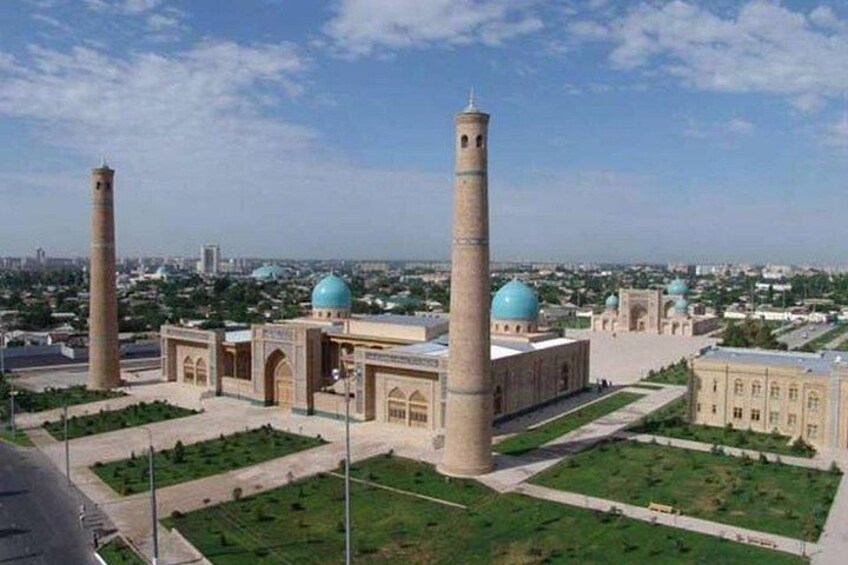 A mosque with two minarets and blue domes, surrounded by green lawns and a cityscape in the background. 2