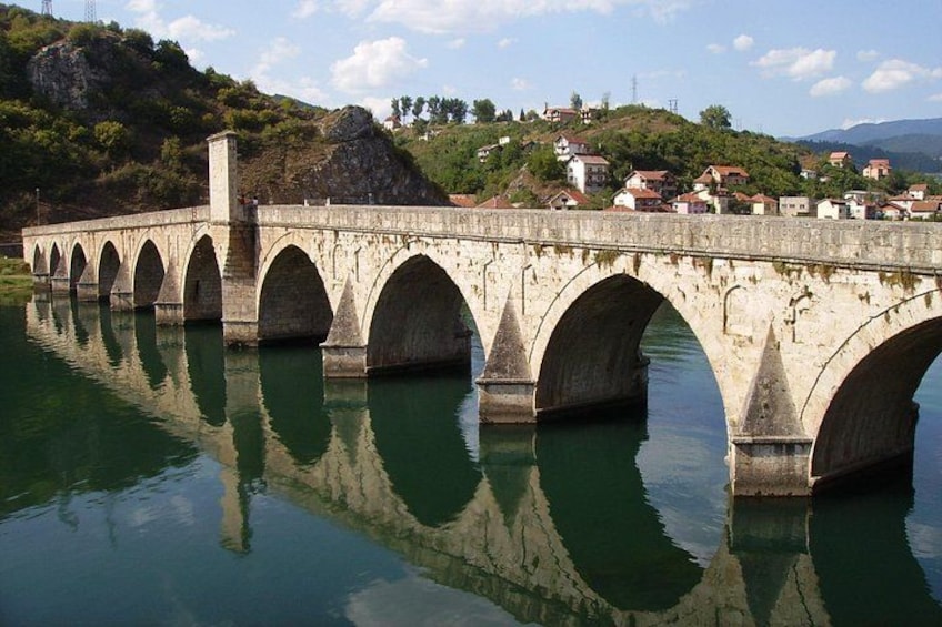 A stone bridge with multiple arches over a body of water, surrounded by hills and houses. 5