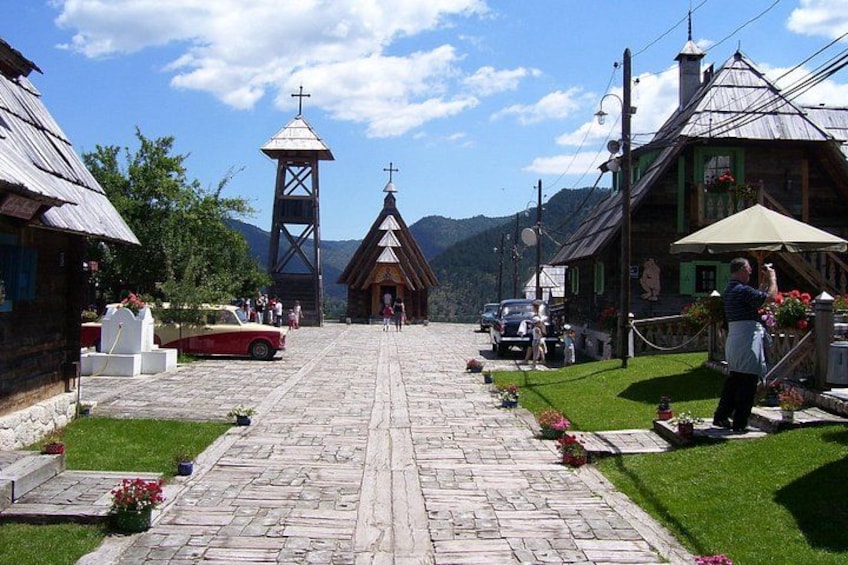 A cobblestone path leading to a church with a bell tower, surrounded by traditional buildings and a mountainous backdrop. 4