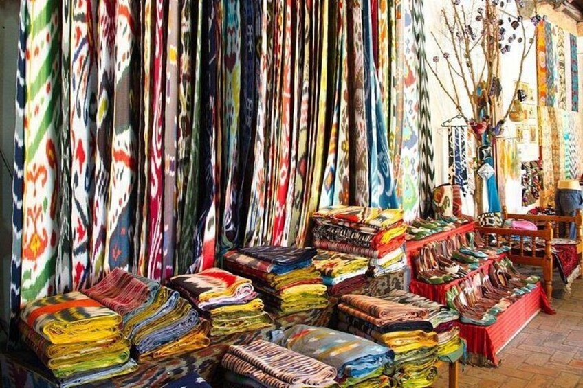 A market with colorful fabrics displayed on tables and hanging on walls. 1
