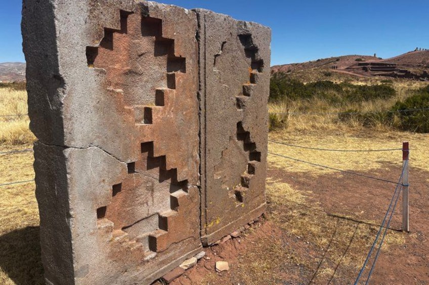 Una gran estructura de piedra con diseños labrados, rodeada de hierba seca y un cielo despejado. 1