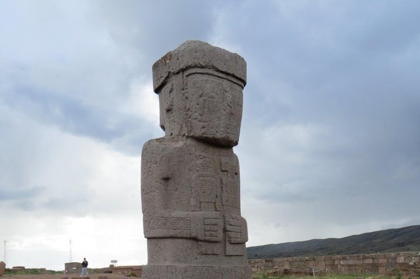 Un grand monolithe de pierre orné de sculptures, se dressant sur un arrière-plan de ciel nuageux et d’un paysage vallonné. 2