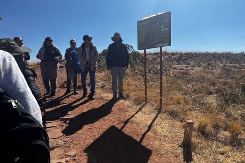 Un grupo de personas de pie sobre un sendero de tierra en un paisaje seco y cubierto de hierba. 5