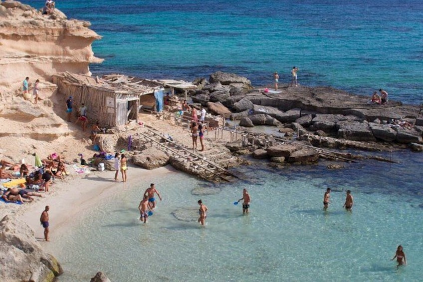 A rocky beach with clear water, people swimming and sunbathing, and a small hut. 2