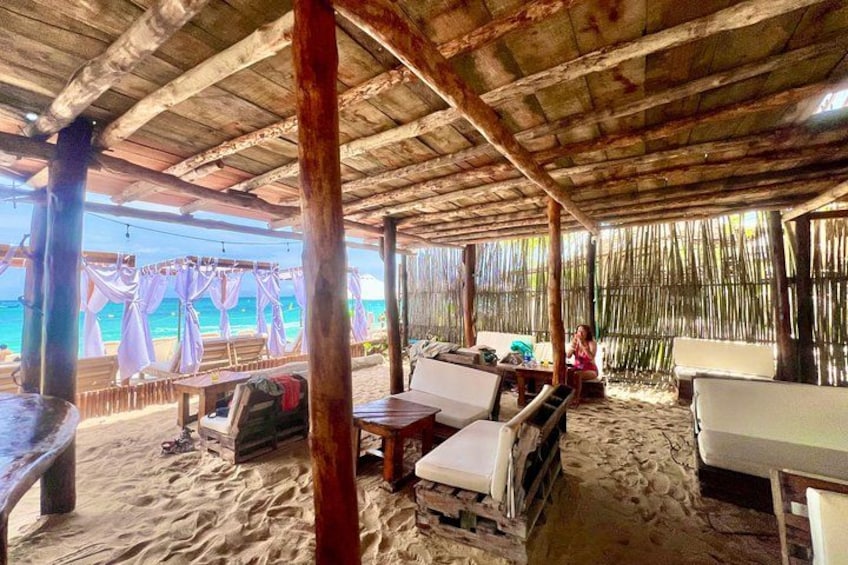A beachside hut with wooden beams, a sandy floor, and a view of the ocean. 2