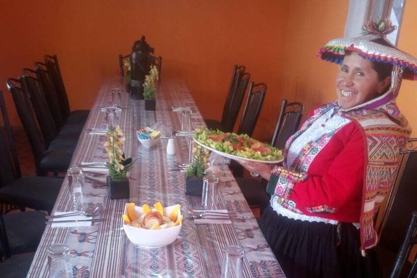 A person in traditional attire holding a plate of food at a dining table with chairs and a vase of flowers. 3