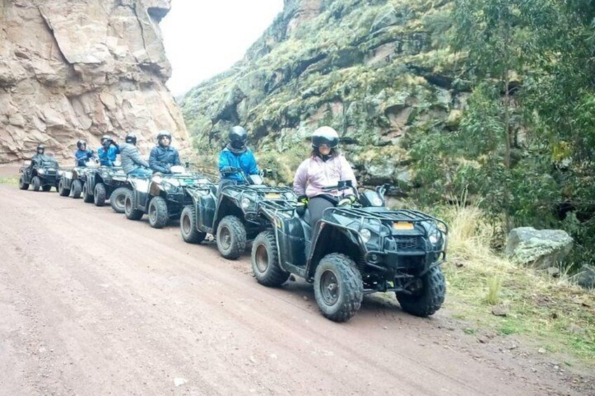 Una fila de cuatrimotos sobre un camino de tierra, con acantilados rocosos y vegetación al fondo. 3
