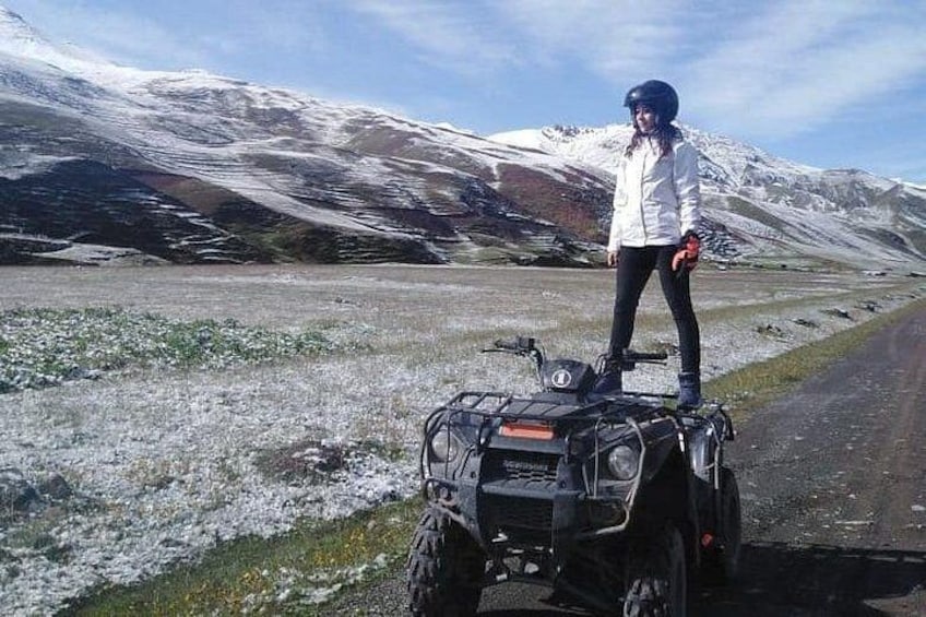 Una persona in moto quad su una strada, con montagne innevate sullo sfondo. 5