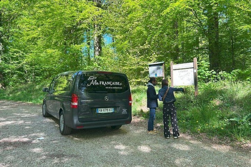 Un coche estacionado en un camino de grava, con dos personas a su lado que observan un cartel. 1