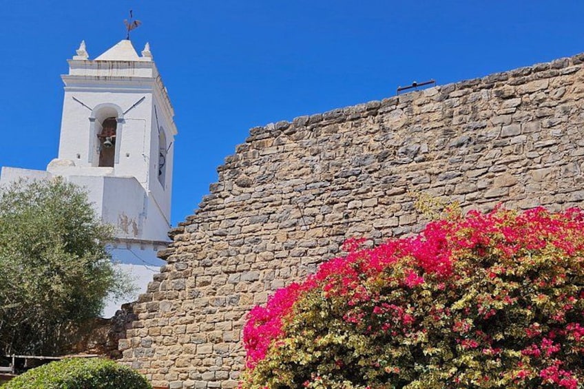 Un muro de piedra, una torre de campanas blanca y flores rosadas. 4