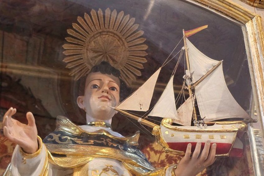 Une statue représentant une figure tenant un modèle de navire, agrémentée de décorations élaborées et d'un motif en forme de rayons de soleil en arrière-plan. 2