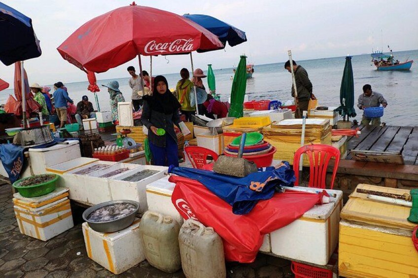 A market scene with people, fishing boats, and various goods on display. 2