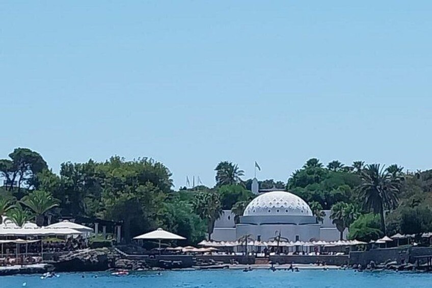 Una gran estructura en forma de cúpula blanca, un cuerpo de agua y una playa con sombrillas. 5