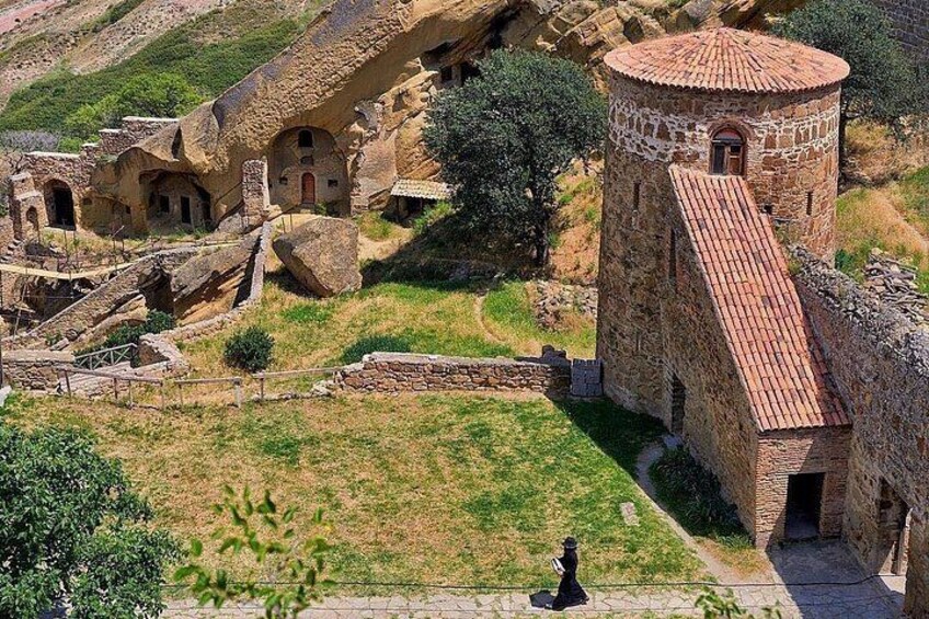 Ancient stone buildings with a tower, a paved walkway, and a grassy area. 5