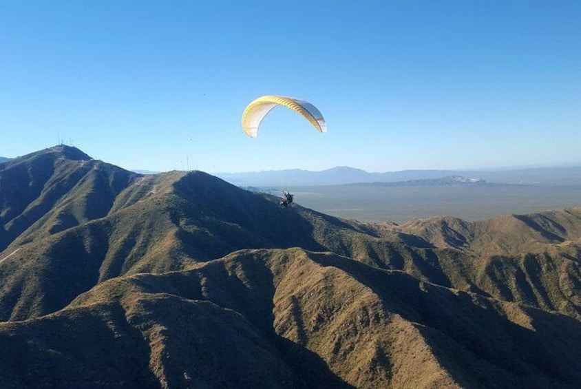 Una persona practicando parapente sobre un paisaje montañoso con cielos despejados. 1