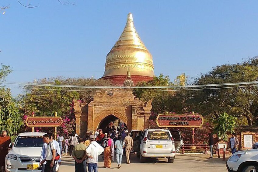 A golden stupa with a brick gateway, surrounded by trees and people. 5