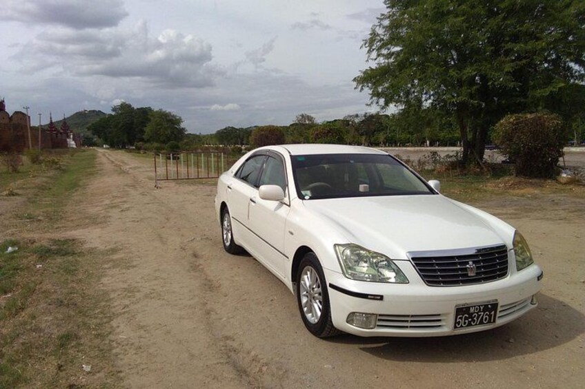 A white car parked on a dirt road with a fence and trees in the background. 1