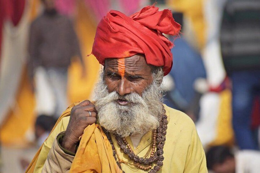 A person wearing a red turban and yellow traditional attire, with a beaded necklace. 1