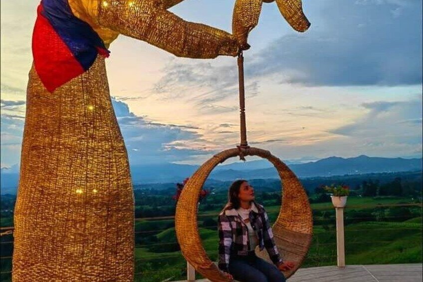 A person sitting in a wicker chair suspended by a rope, with a golden structure in the background. 5