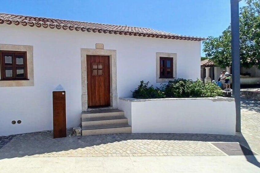 Un edificio blanco con puerta y ventanas marrones, una pequeña escalera y un área pavimentada con un muro de piedra. 2