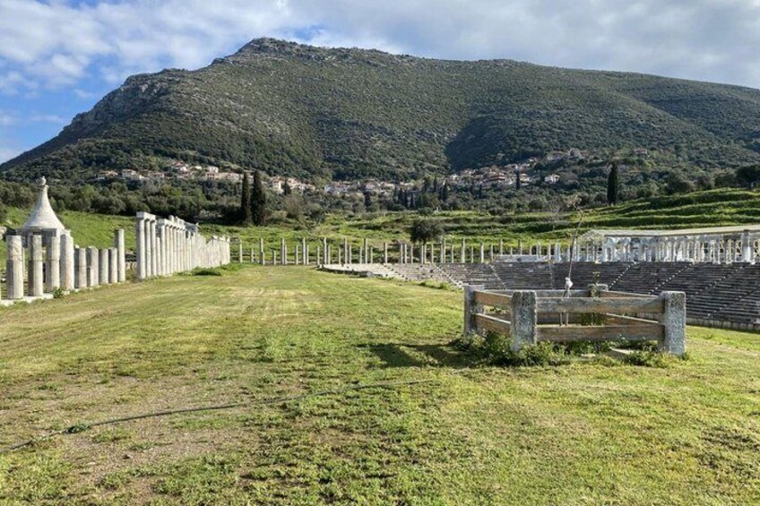 A historical amphitheater with ruins, a grassy field, and a mountain in the background. 2