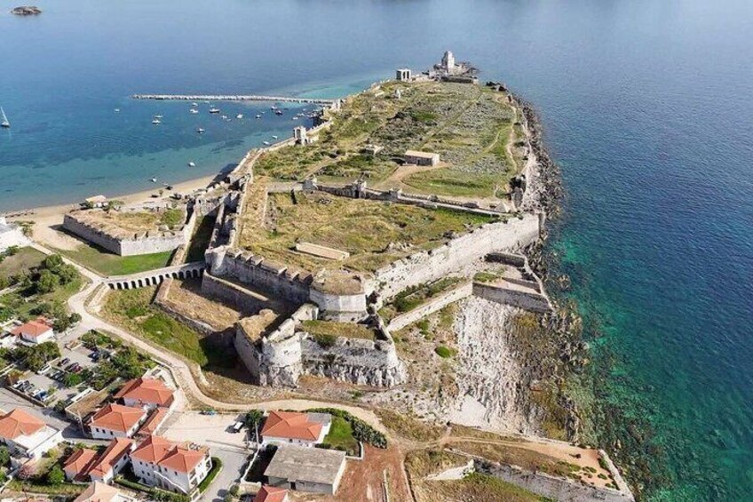 A coastal fortification with a lighthouse, clear blue sea, and surrounding residential area. 5