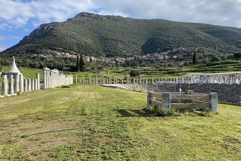 A historical site with ruins, a large open field, and a mountain in the background. 2